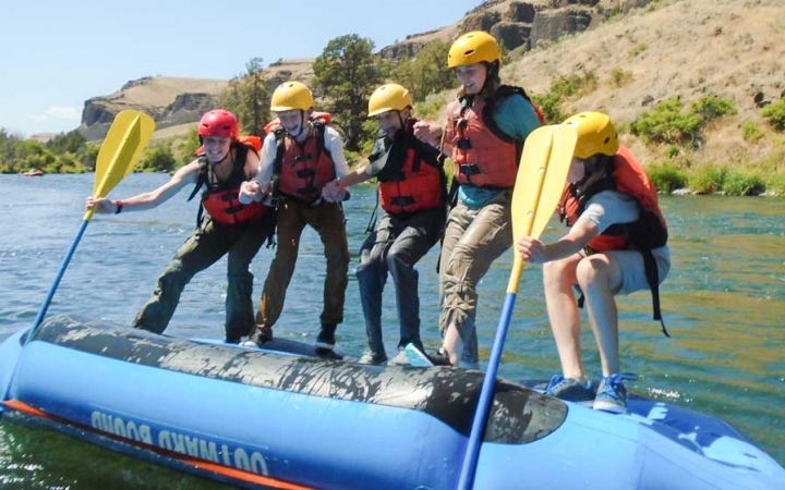 a group of outward bound students stand on the underside of a raft during a rafting exercise 
